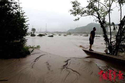 村民站在河岸边围观汹涌的洪水